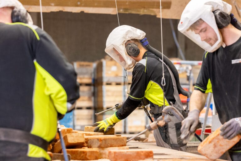 Arbejdere med sikkerhedsudstyr håndterer mursten på fabrik